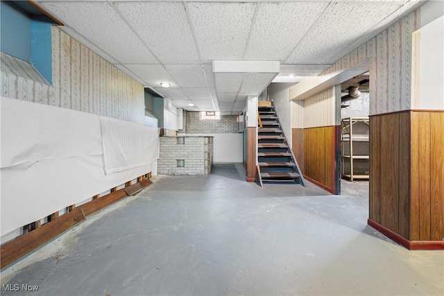 finished basement featuring stairs, wood walls, wainscoting, and a drop ceiling