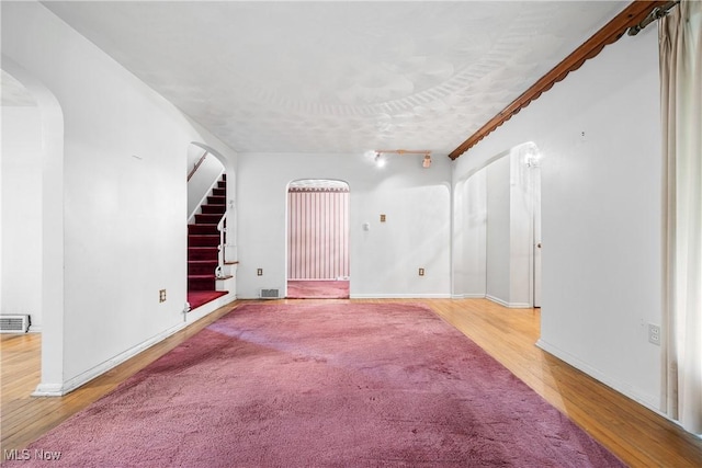 unfurnished living room featuring visible vents, stairs, wood finished floors, baseboards, and arched walkways