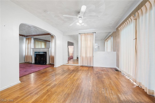 unfurnished living room with visible vents, a fireplace, ceiling fan, hardwood / wood-style flooring, and arched walkways