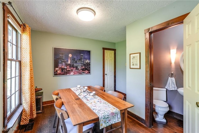 dining area featuring dark wood-type flooring, a textured ceiling, baseboards, and a healthy amount of sunlight