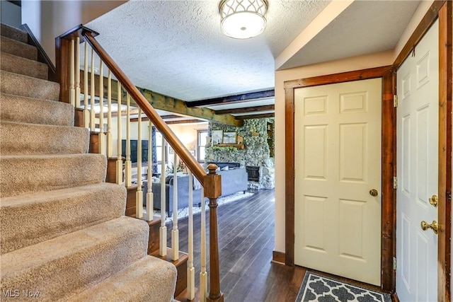 foyer featuring a fireplace, a textured ceiling, stairs, dark wood-type flooring, and beamed ceiling