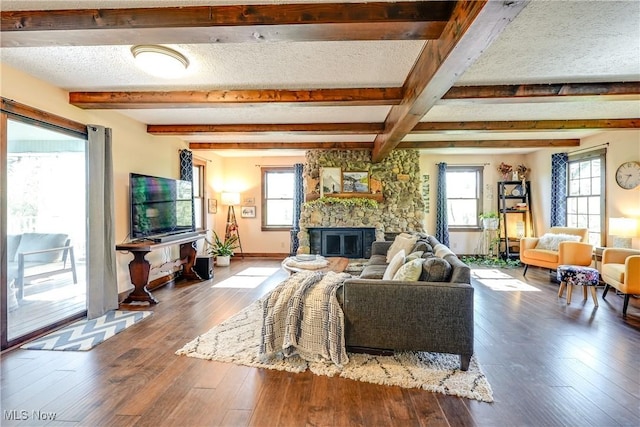 living room with a stone fireplace, baseboards, hardwood / wood-style floors, and beamed ceiling