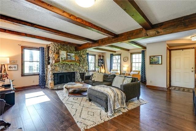 living area with beamed ceiling, baseboards, a stone fireplace, a textured ceiling, and dark wood finished floors
