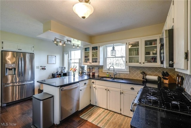 kitchen featuring a textured ceiling, dark countertops, a sink, a peninsula, and stainless steel appliances