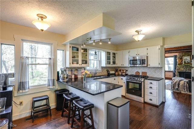 kitchen featuring a peninsula, gas range oven, a textured ceiling, stainless steel microwave, and a sink