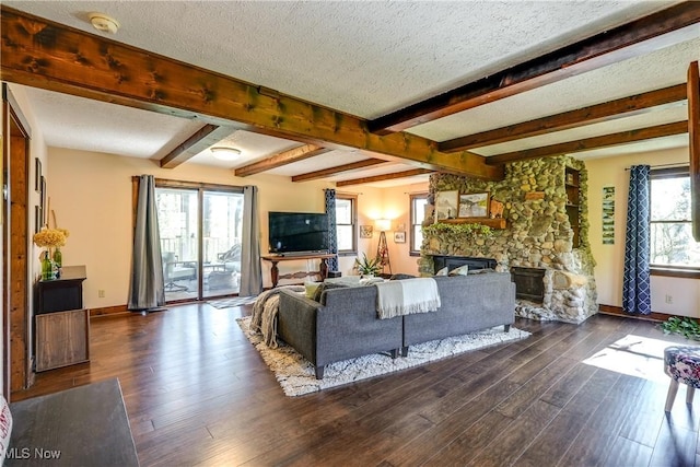 living area with a stone fireplace, a textured ceiling, dark wood-style flooring, and baseboards