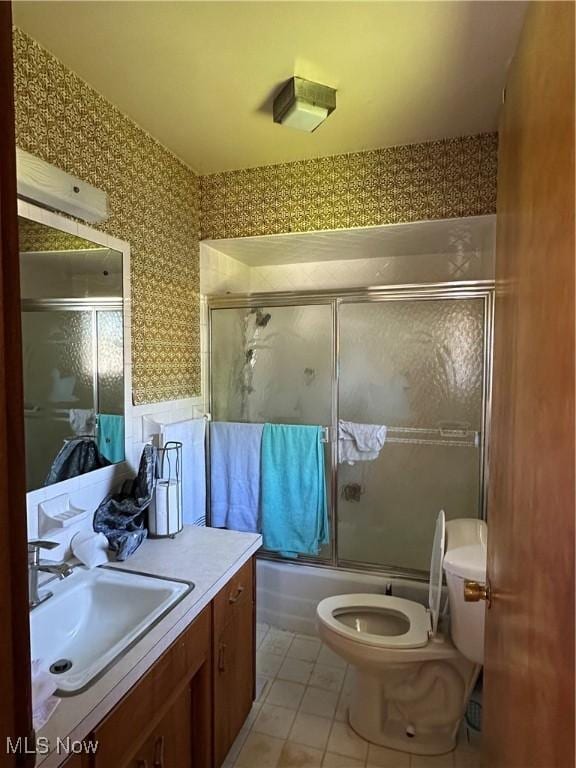 full bath featuring vanity, enclosed tub / shower combo, toilet, and wallpapered walls