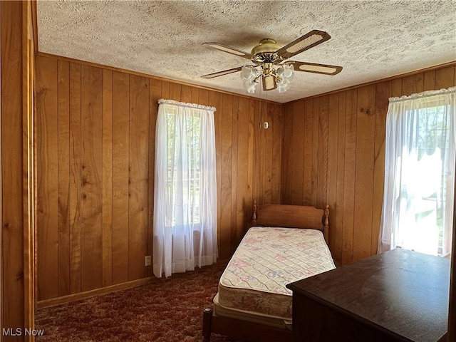 carpeted bedroom with wooden walls, ceiling fan, and a textured ceiling