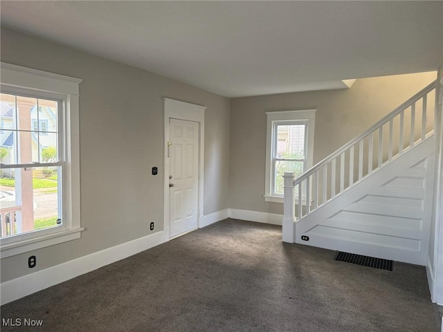 foyer entrance featuring baseboards, visible vents, dark carpet, and stairway