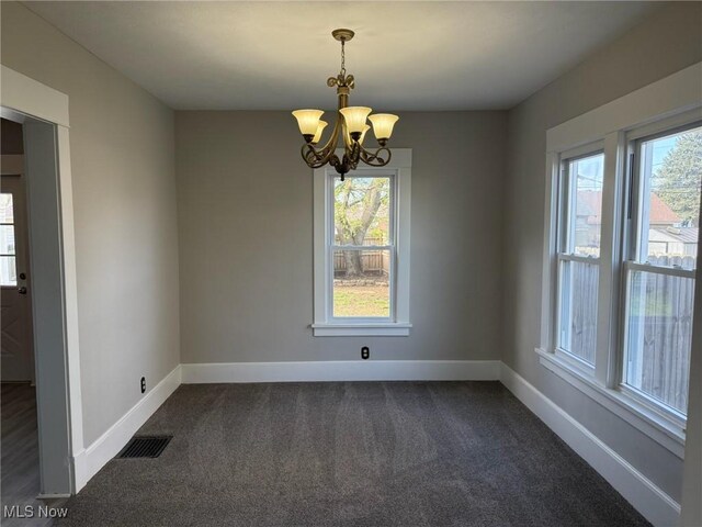 unfurnished dining area featuring dark carpet, baseboards, a notable chandelier, and visible vents