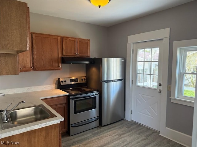 kitchen with appliances with stainless steel finishes, a sink, light countertops, brown cabinetry, and under cabinet range hood