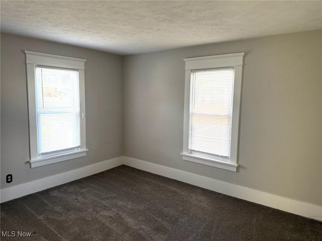 spare room with baseboards, a textured ceiling, and dark carpet