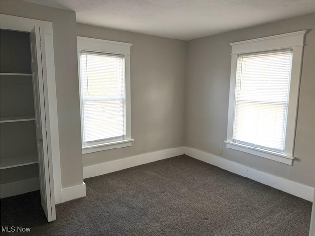 unfurnished bedroom featuring baseboards, multiple windows, and dark colored carpet