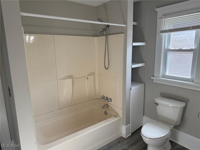 bathroom with baseboards, washtub / shower combination, wood finished floors, and toilet