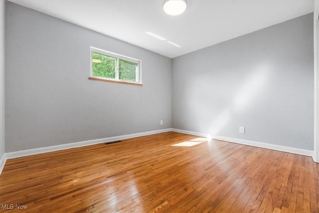 empty room with visible vents, light wood finished floors, and baseboards