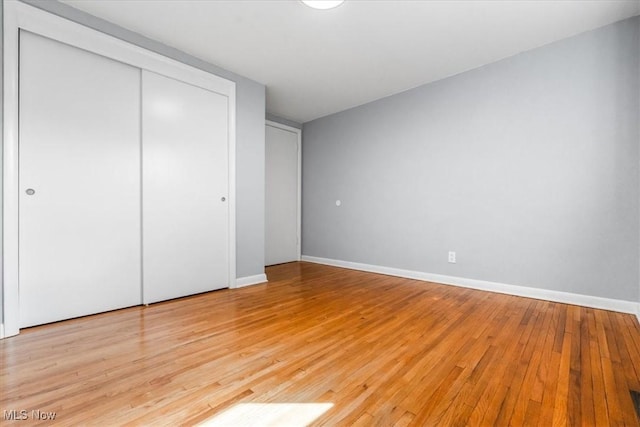 unfurnished bedroom featuring baseboards, light wood-style flooring, and a closet