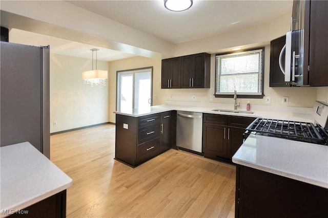 kitchen featuring light wood-type flooring, a sink, a peninsula, and stainless steel appliances