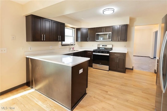 kitchen featuring a sink, light countertops, a peninsula, stainless steel appliances, and light wood-style flooring