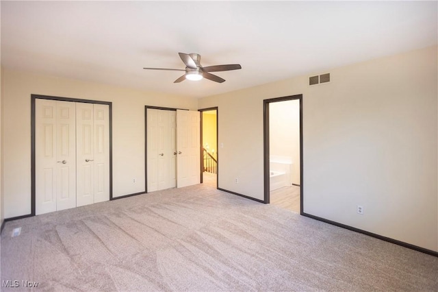 unfurnished bedroom with carpet flooring, connected bathroom, two closets, baseboards, and visible vents