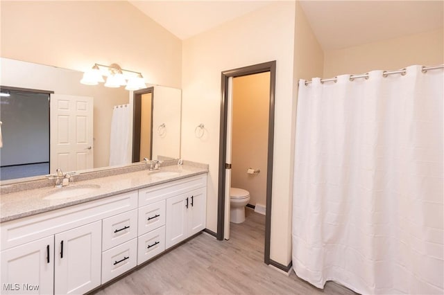 full bath featuring double vanity, a sink, wood finished floors, and toilet