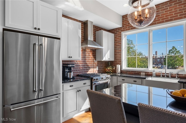 kitchen featuring wall chimney range hood, dark stone counters, white cabinetry, decorative backsplash, and premium appliances