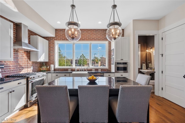 kitchen with a sink, a breakfast bar area, wall chimney range hood, and stainless steel appliances