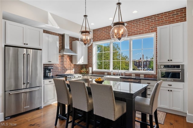 kitchen with wall chimney range hood, white cabinetry, appliances with stainless steel finishes, and a sink