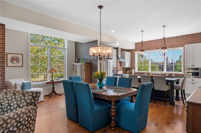 dining space with brick wall, recessed lighting, light wood-style flooring, and a notable chandelier