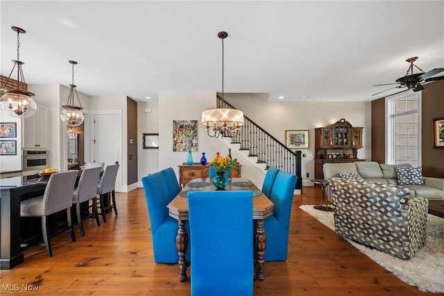 dining room with stairs, baseboards, hardwood / wood-style flooring, and ceiling fan with notable chandelier