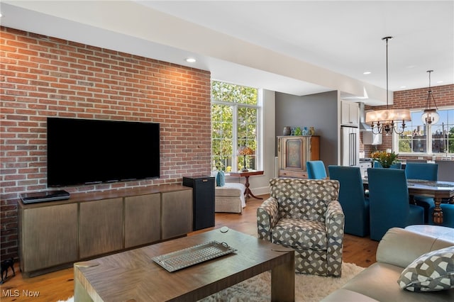 living area featuring an inviting chandelier, recessed lighting, light wood-style floors, and brick wall