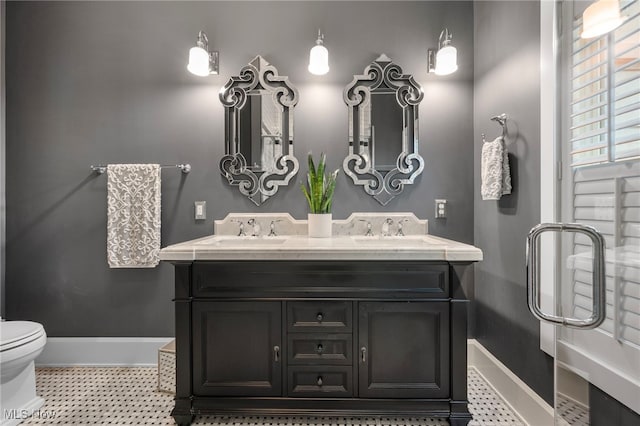 bathroom featuring a sink, baseboards, toilet, and double vanity