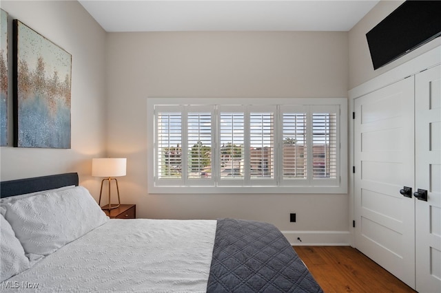 bedroom featuring baseboards, a closet, wood finished floors, and multiple windows