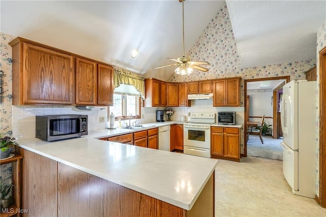 kitchen with white appliances, light countertops, under cabinet range hood, a sink, and vaulted ceiling