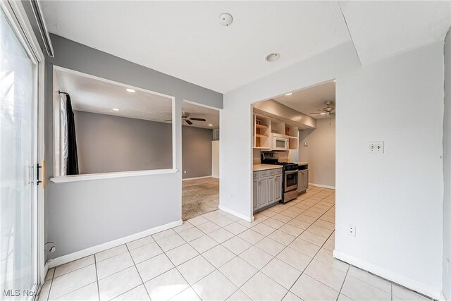 kitchen with a ceiling fan, stainless steel gas stove, baseboards, white microwave, and light tile patterned flooring