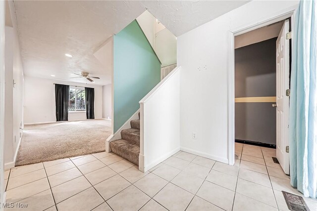 staircase with ceiling fan, visible vents, tile patterned flooring, baseboards, and carpet