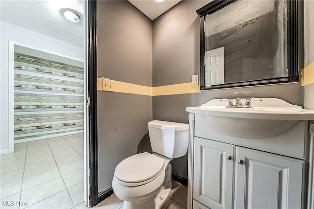 half bath featuring baseboards, tile patterned floors, vanity, and toilet