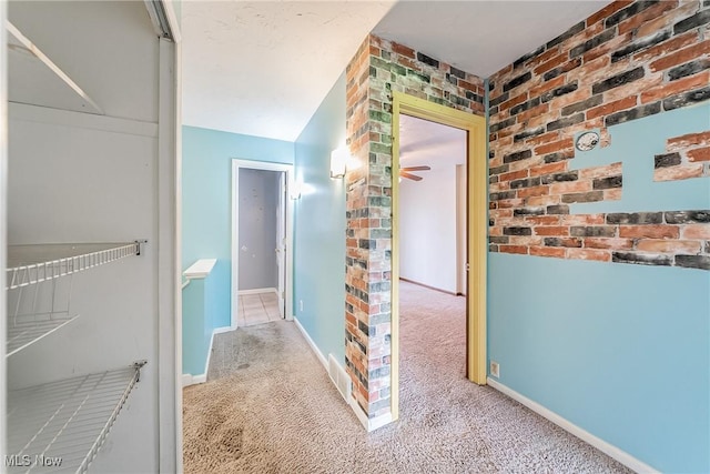 hallway with carpet flooring, brick wall, visible vents, and baseboards