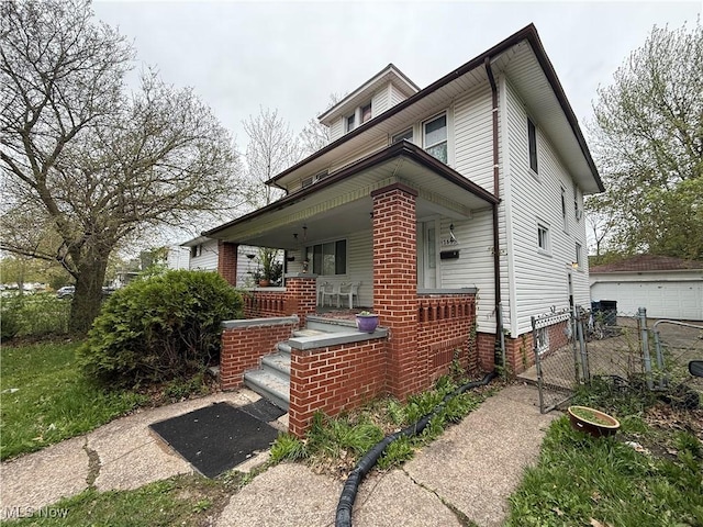 american foursquare style home with covered porch, fence, a gate, and a detached garage