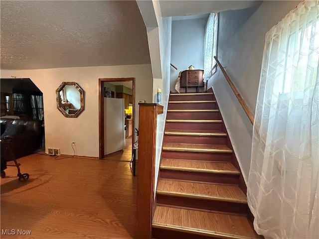 stairway featuring a textured ceiling, arched walkways, and wood finished floors