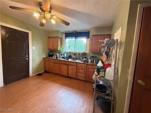 kitchen with brown cabinets, ceiling fan, a sink, and light wood finished floors
