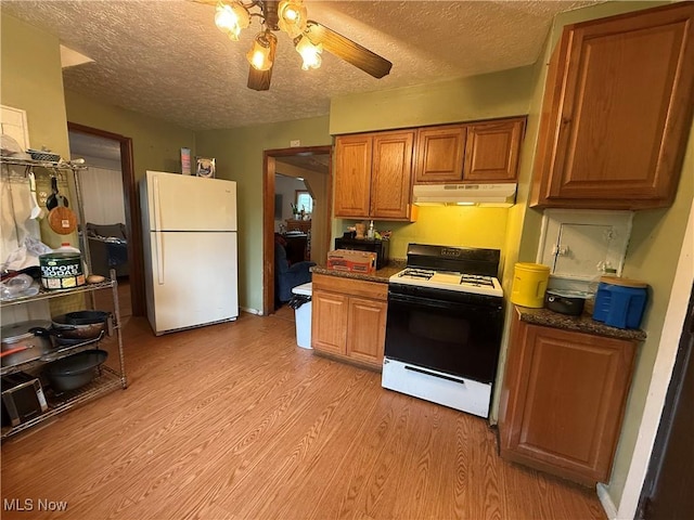 kitchen featuring light wood finished floors, a textured ceiling, range with gas stovetop, freestanding refrigerator, and under cabinet range hood