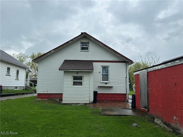 back of house with a lawn, roof with shingles, and a patio area