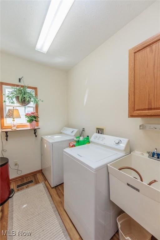 laundry room featuring a sink, washing machine and dryer, light wood-type flooring, and cabinet space