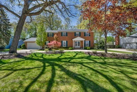colonial inspired home with driveway, stucco siding, french doors, and a front yard