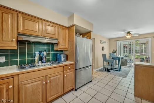 kitchen featuring ceiling fan, appliances with stainless steel finishes, tasteful backsplash, light countertops, and under cabinet range hood