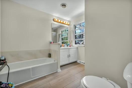 bathroom with a garden tub, visible vents, wood finished floors, vanity, and toilet