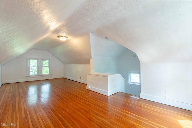 additional living space featuring baseboards, a textured ceiling, vaulted ceiling, and a wealth of natural light