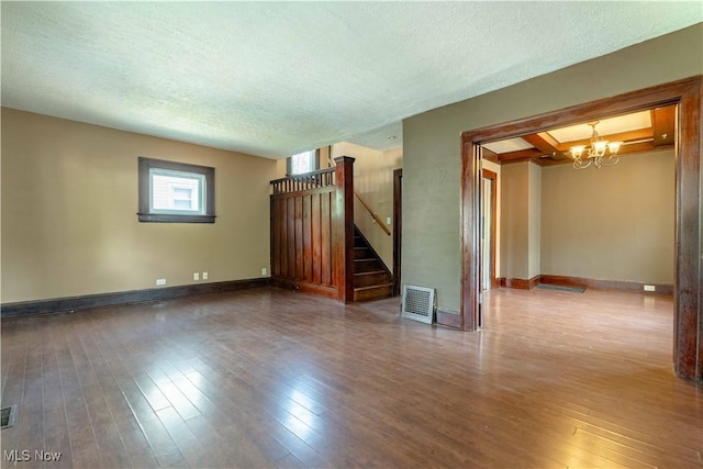 unfurnished living room featuring visible vents, an inviting chandelier, stairway, a textured ceiling, and hardwood / wood-style flooring