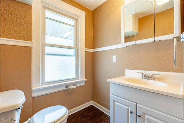 half bathroom with vanity, baseboards, wood finished floors, and toilet