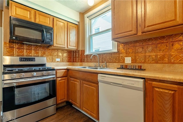 kitchen featuring black microwave, white dishwasher, stainless steel gas range oven, light countertops, and a sink